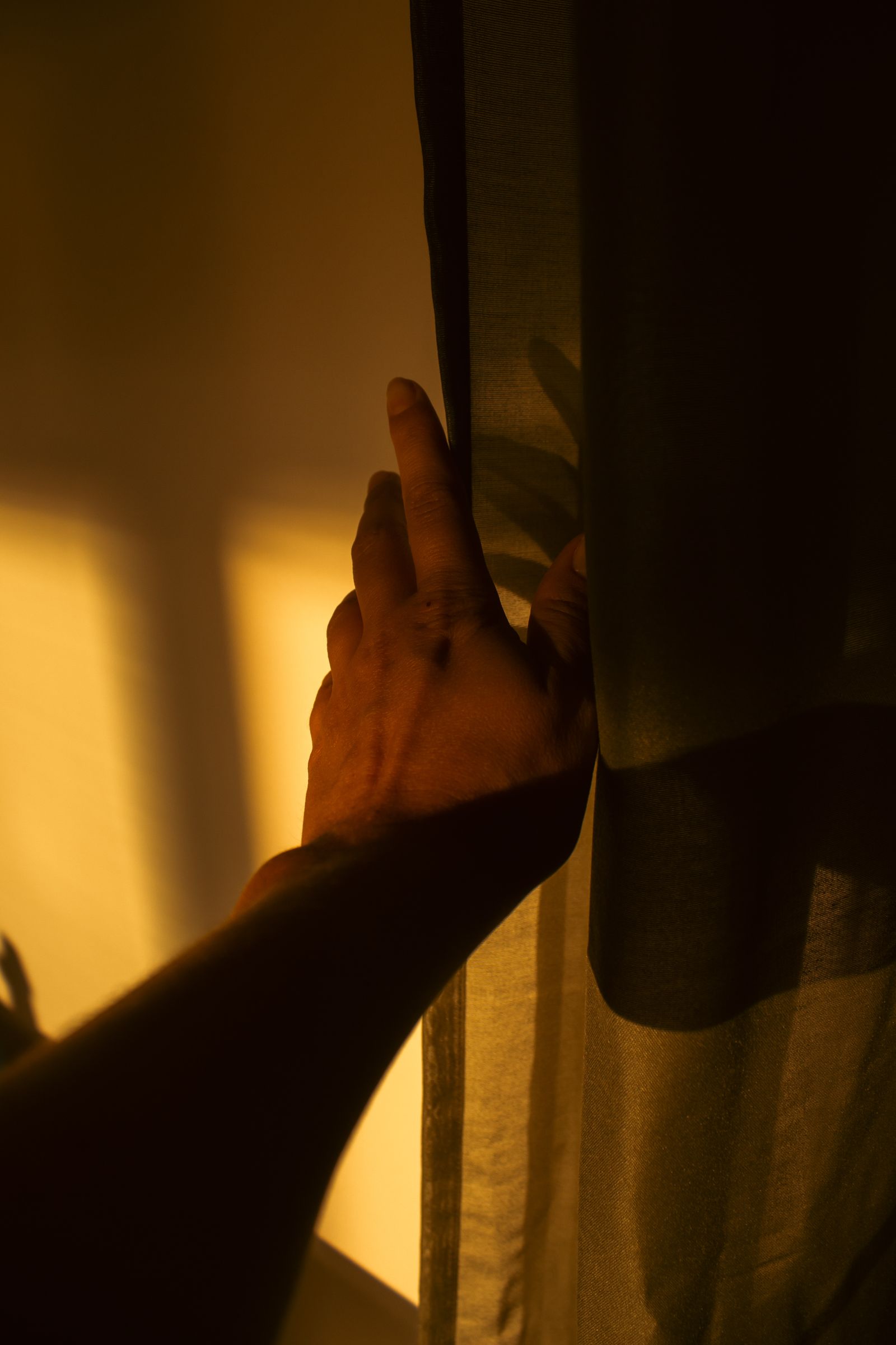 Hand schiebt morgens einen Vorhang beiseite, warmes Sonnenlicht fällt herein