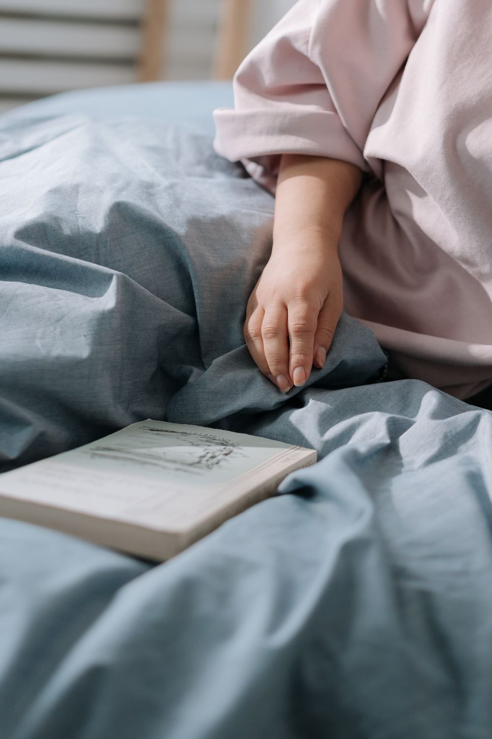 Hand ruht auf der Bettdecke neben einem aufgeschlagenen Buch