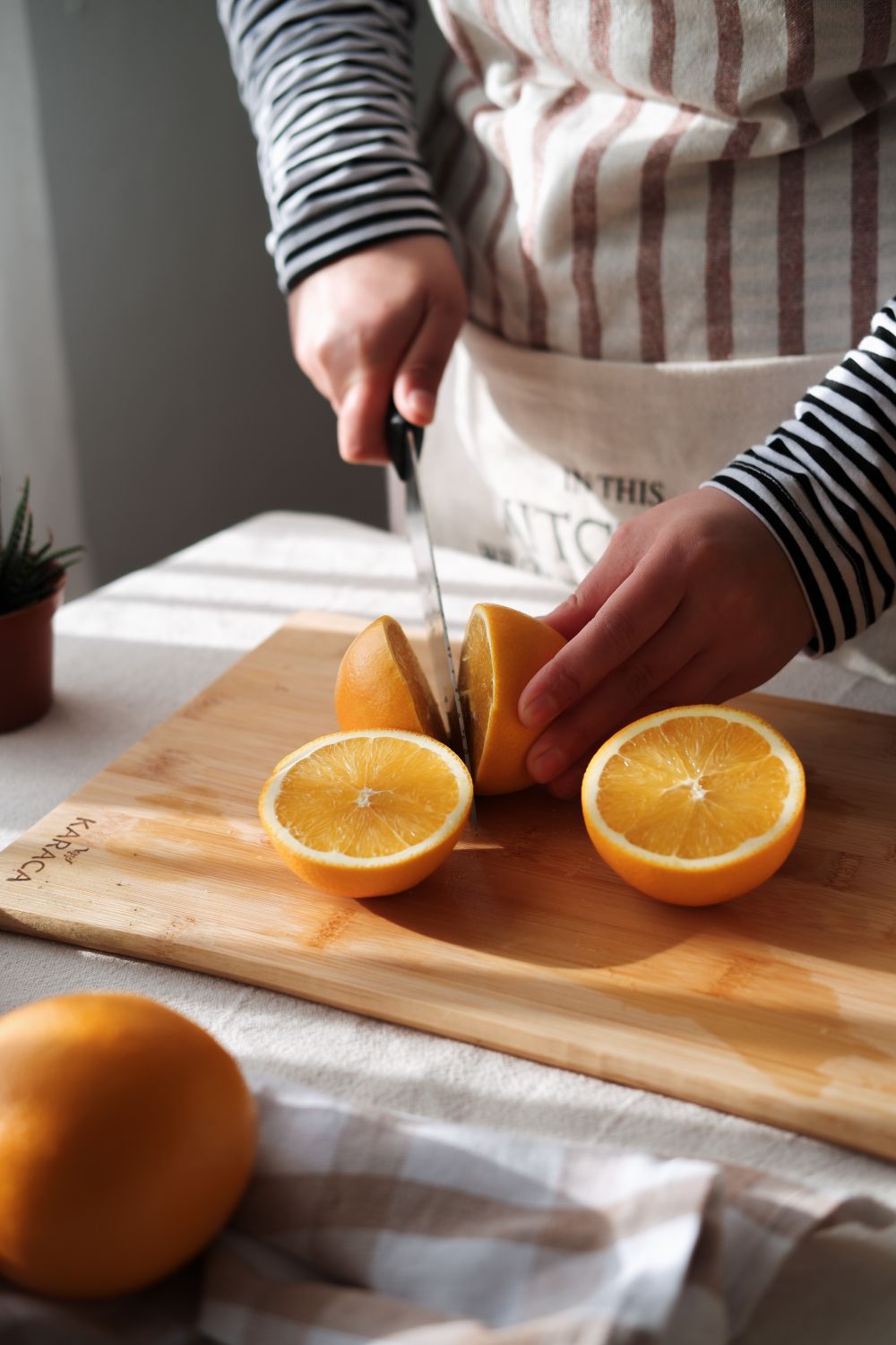 Hände schneiden eine frische Orange auf einem Holzbrett